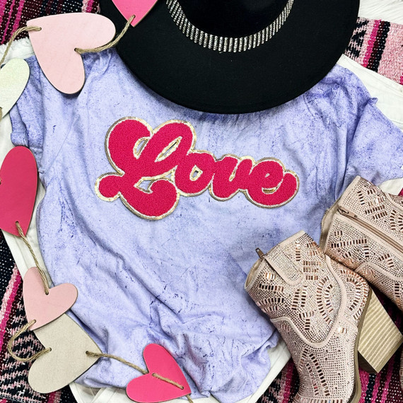 Hot Pink Love Chenille Patch, pink and gold embroidered patch with the word 'Love' on a purple marble-textured t-shirt surrounded by pink and white heart-shaped decorations, beige cut-out sandals with intricate cut-out design and a chunky heel.