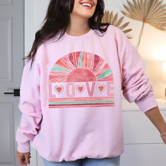 Love Boho DTF Heat Transfer, woman wearing a pink sweatshirt with a colorful sunrise and the word 'LOVE' in decorative letters.