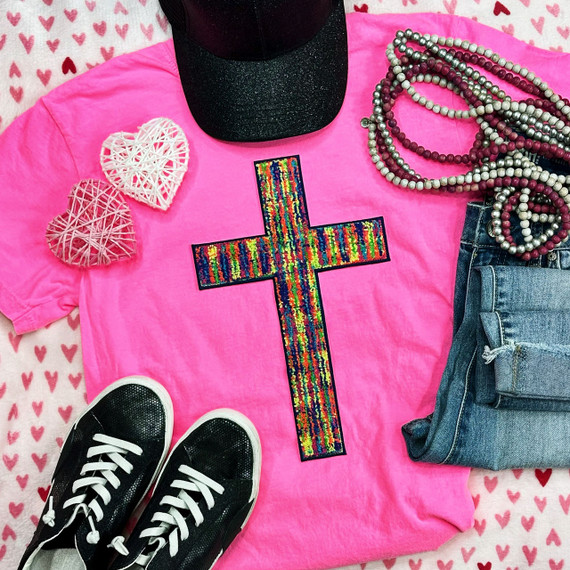 Tie Dye Cross Chenille Patch, colorful embroidered cross patch on a pink t-shirt with heart pattern background, paired with black sneakers, denim jeans, pearl necklaces, and decorative wicker hearts.