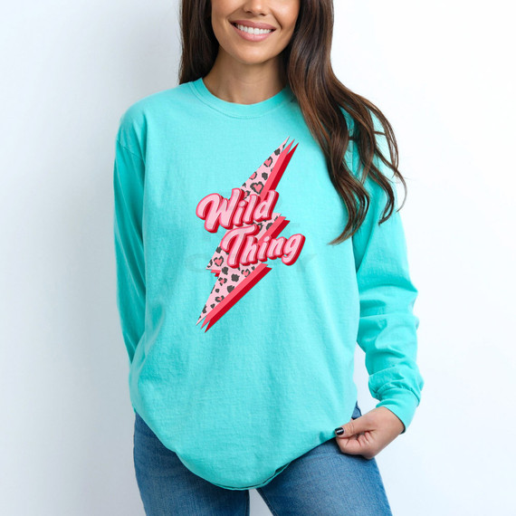 Wild Thing Leopard Bolt DTF Heat Transfer, colorful leopard print lightning bolt with bold pink and red text 'Wild Thing' on a woman wearing a turquoise sweatshirt.