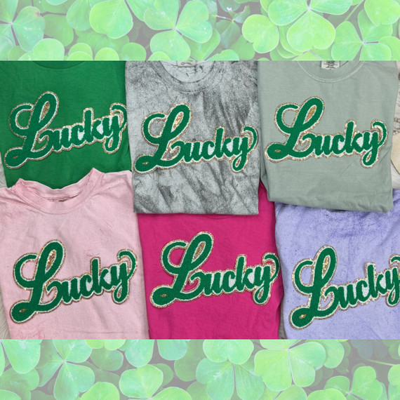 Lucky Chenille Patch, collection of colorful casual t-shirts featuring the word Lucky embroidered with green and gold chenille patches in various colors including pink, grey, green, purple, and light pink.