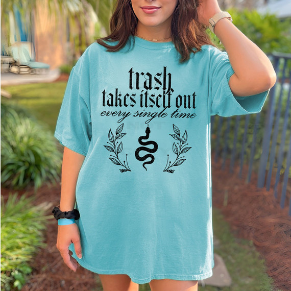 Trash Takes Itself Out Every Single Time Snake DTF Heat Transfer, a woman wearing a blue t-shirt with a black snake and leaf design and humorous quote printed on it in an outdoor setting.