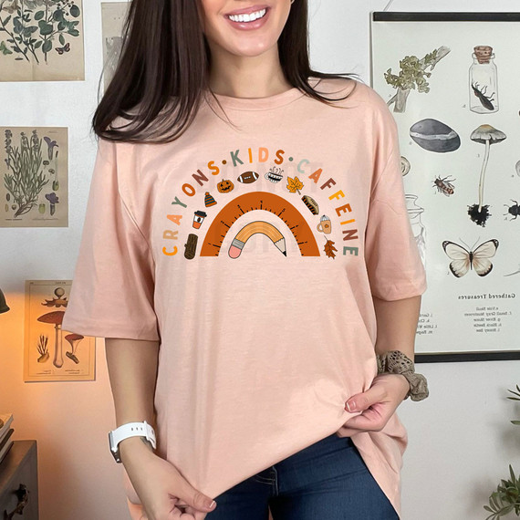 Teacher Fall Rainbow DTF Heat Transfer, a colorful graphic on a light pink T-shirt featuring fall themes like leaves, pumpkins, and cozy items, designed for kids and teachers.