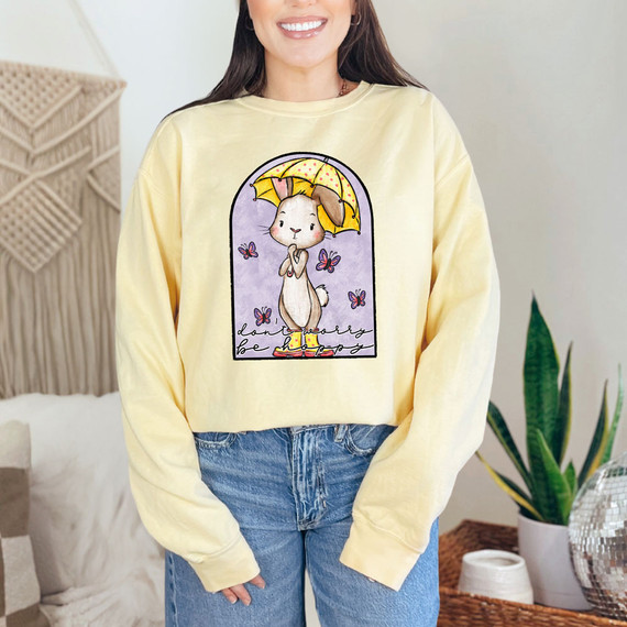 Don't Worry Be Hoppy Classic Bunny DTF Heat Transfer, a cute bunny holding an umbrella with butterflies around it on a yellow sweatshirt.