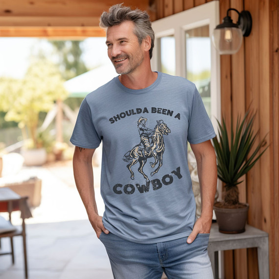 Shoulda Been A Cowboy DTF Heat Transfer, printed on a light blue T-shirt featuring a cowboy riding a bucking horse and the text "Shoulda Been A Cowboy".