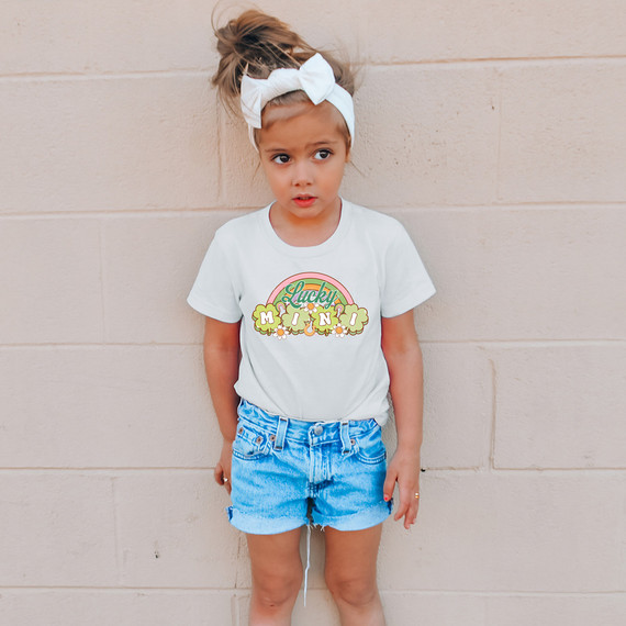 Lucky Mini Shamrocks DTF Heat Transfer, colorful small shamrock design with the words 'Lucky Mini' on a white t-shirt worn by a girl.