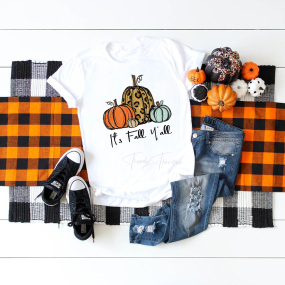 It's Fall Y'all Pumpkins Sublimation Transfer, a white t-shirt with colorful pumpkins and the phrase 'It's Fall Y'all' printed on it, surrounded by fall-themed decorations including mini pumpkins, gourds, and autumnal accents.