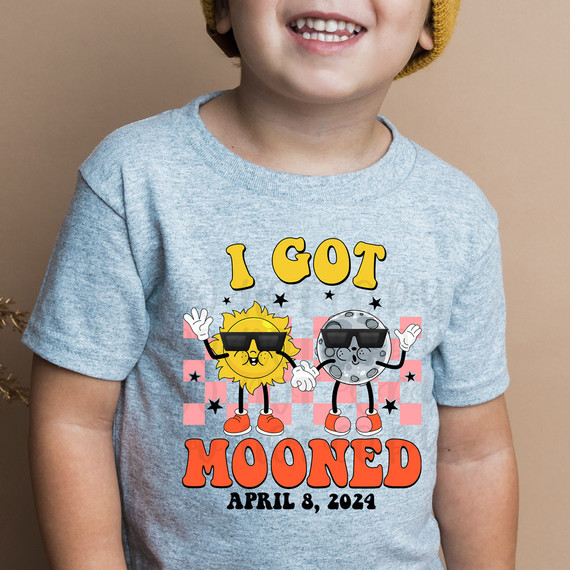 I Got Mooned DTF Heat Transfer, a colorful graphic design featuring a smiling sun and moon wearing sunglasses, with the text "I Got Mooned" and the date April 8, 2024, on a child's T-shirt.