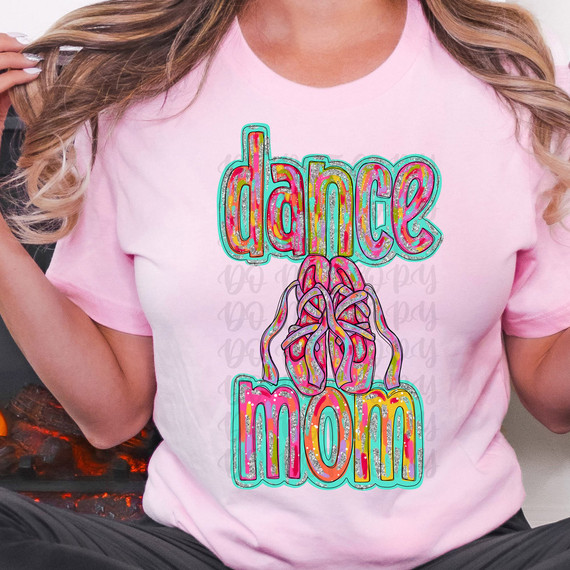 Dance Mom Glitz DTF Heat Transfer, colorful glittery design of the word 'dance' and an illustration of hands holding a heart-shaped object, printed on a pink t-shirt.