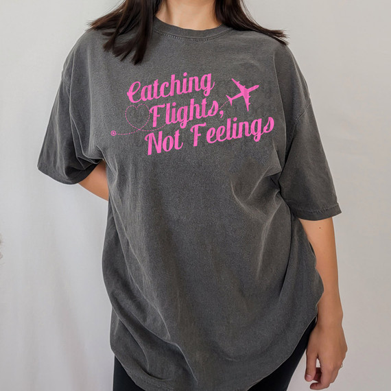 Catching Flights, Not Feelings DTF Heat Transfer design on a gray T-shirt, with pink text and airplane graphics.