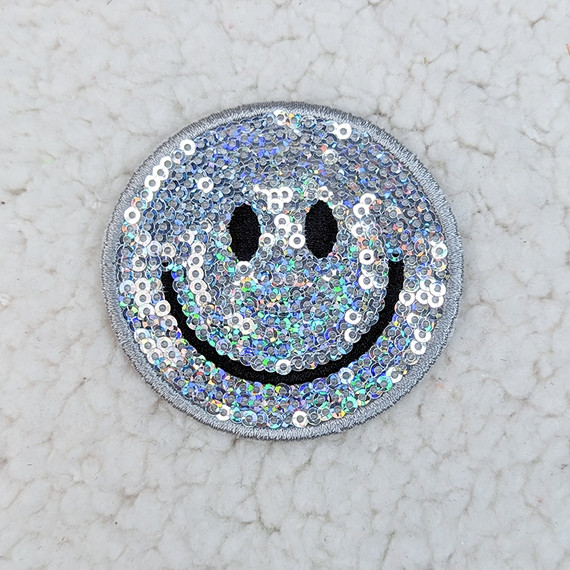 SILVER Sequin Happy Face HAT/POCKET Patch, a circular patch featuring a smiling face design made of shiny silver sequins with black embroidered details for the eyes and mouth.