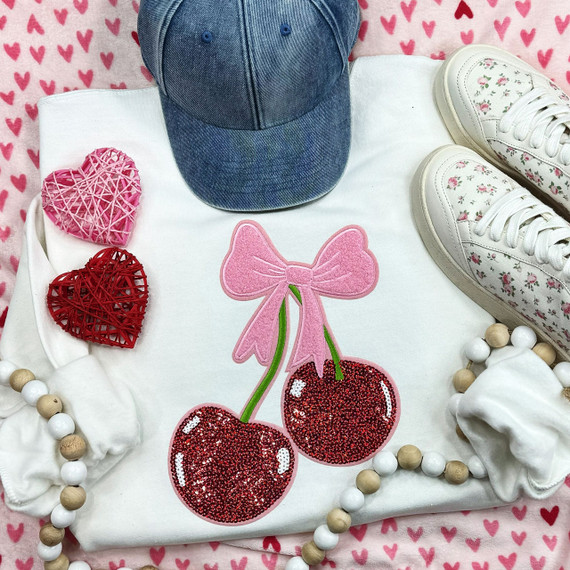 Double Cherries with Bow Chenille Sequin Patch, pink bow with red cherry design embroidered on fabric background with denim cap, white sneakers with floral pattern, and decorative hearts and beads