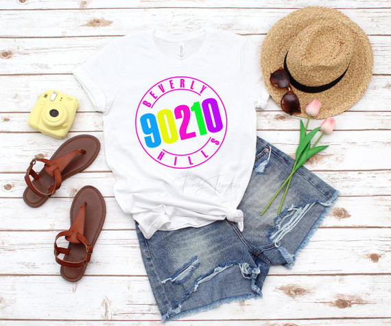 90210 Beverly Hills fan art Sublimation Transfer T-shirt, casual white t-shirt with colorful Beverly Hills 90210 logo, denim shorts, straw hat, sunglasses, tulips, yellow instant camera, brown sandals, summer accessories.