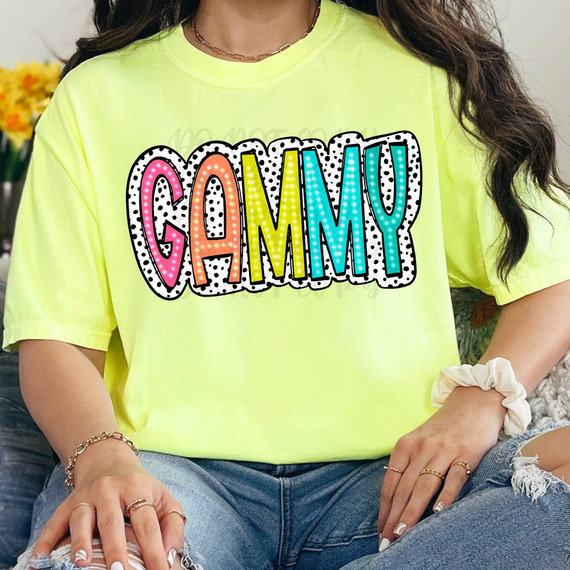 Gammy Dalmatian Dots DTF Heat Transfer, colorful multicolored letters spelling 'GAMMY' with Dalmatian dots pattern on a yellow T-shirt.