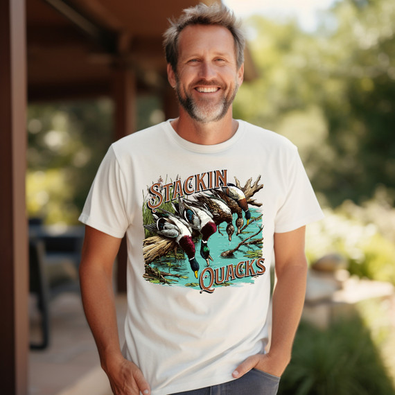 Stackin' Quacks DTF Heat Transfer product, colorful duck-themed design of ducks hanging over water with the text 'Stackin' Quacks' on a white T-shirt worn by a smiling man outdoors.
