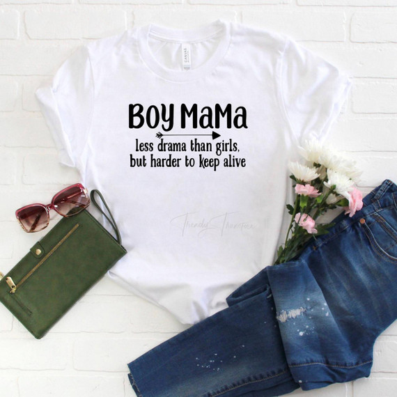 Boy MaMa Less Drama Than Girls But Harder to Keep Alive Sublimation Transfer - White T-Shirt with black text and arrow design, surrounded by sunglasses, a green clutch, denim jeans, and pink and white flowers.