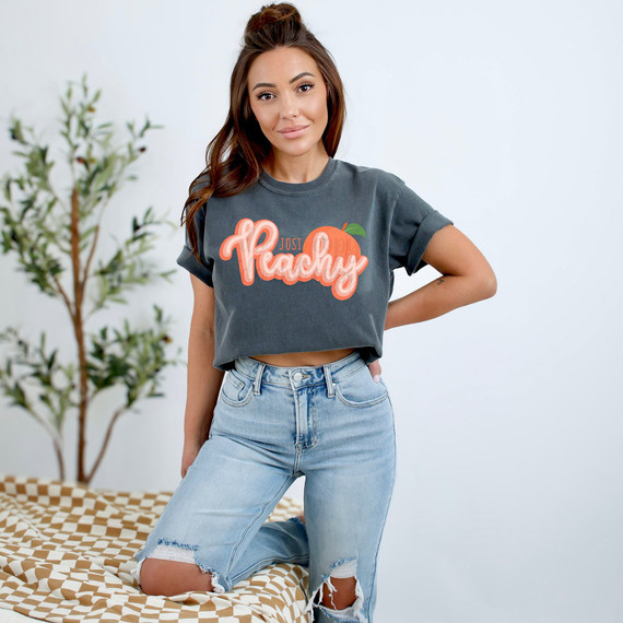 Just Peachy Distressed DTF Heat Transfer, a woman wearing a grey T-shirt with the 'Just Peachy' design featuring a peach graphic and vibrant lettering.