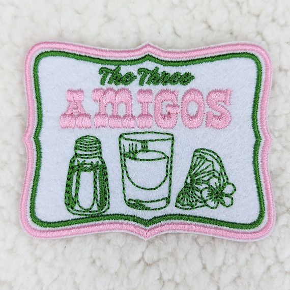 The Three Amigos Embroidered HAT/POCKET Patch, decorative fabric patch with embroidered text and images of salt, a lime with a flower, and a shot glass outlined in green, pink, and white.