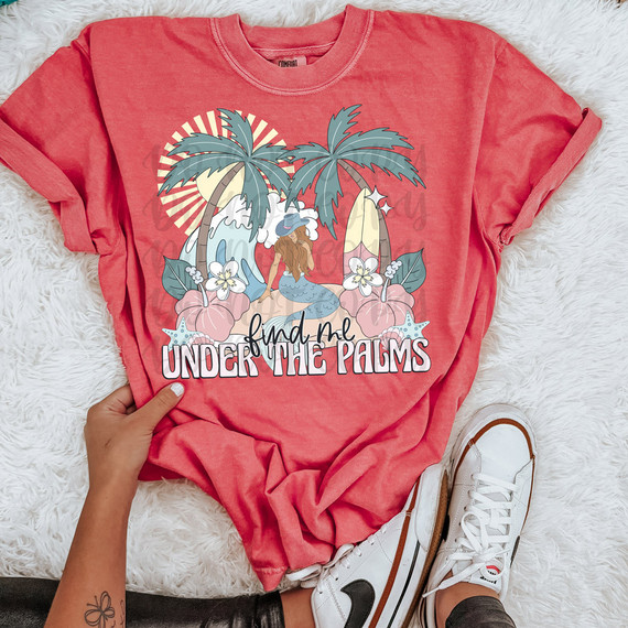 Find Me Under The Palms Muted Retro DTF Heat Transfer, graphic T-shirt with tropical palm trees, waves, a mermaid, and floral design on pink fabric.