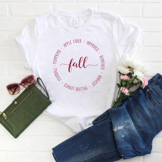Fall Text circle Sublimation Transfer, a white T-shirt with a fall-themed circular text design and the word 'fall' in the center, surrounded by words like pumpkin, apple cider, hayrides, bonfires, harvest, football, and fall.