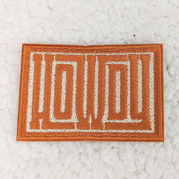 Howdy Embroidered HAT/POCKET Patch, orange fabric patch with white embroidered outline of the word 'Howdy'.