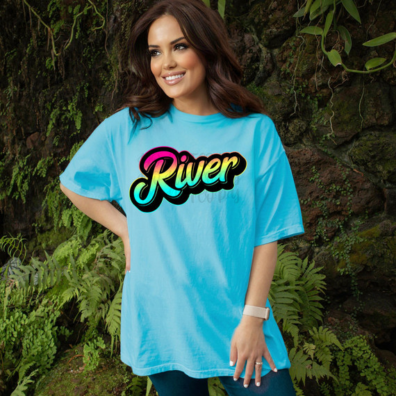 River Rainbow Gradient DTF Heat Transfer, colorful rainbow gradient text on a light blue T-shirt worn by smiling woman in outdoor setting.