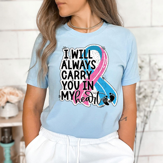 I Will Always Carry You In My Heart DTF Heat Transfer, woman wearing a light blue t-shirt with a sentimental and colorful design featuring a pink and blue ribbon, heartfelt message, and black paw prints.