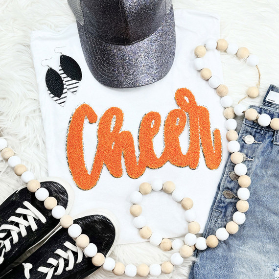 Cursive Cheer Orange Chenille Patch, bright orange embroidered cheer word patch on white t-shirt with accessories including black sneakers, earrings, beaded necklace, and denim jeans.