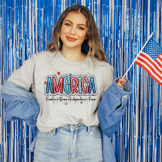 America Faux Sequins DTF Heat Transfer, a glittery and colorful decal design on a sweatshirt featuring the word 'America' with patriotic themes, suitable for customizing apparel.