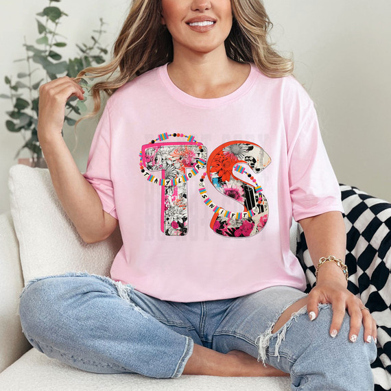 TS Floral DTF Heat Transfer, colorful floral letter design on a pink T-shirt worn by a woman sitting on a sofa.