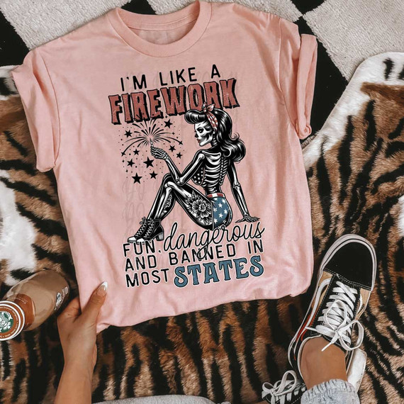 I'm Like A Firework DTF Heat Transfer, pink t-shirt with a skeleton girl holding a firework, with text about being fun, dangerous, and bold in the USA