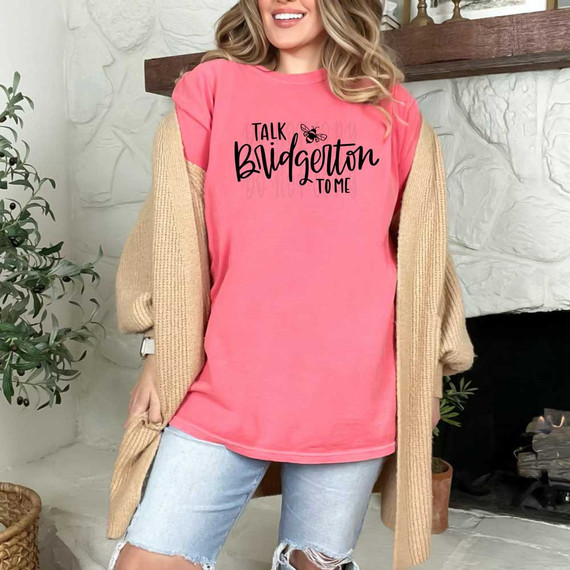 Talk Bridgerton To Me BLACK DTF Heat Transfer, pink t-shirt with black text and a small bee illustration, worn by a smiling woman with blonde hair.