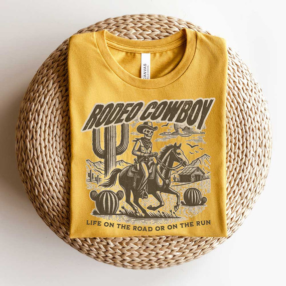 Rodeo Cowboy DTF Heat Transfer, yellow t-shirt with a cowboy riding a horse, cacti, mountains, and desert scenery printed on it.