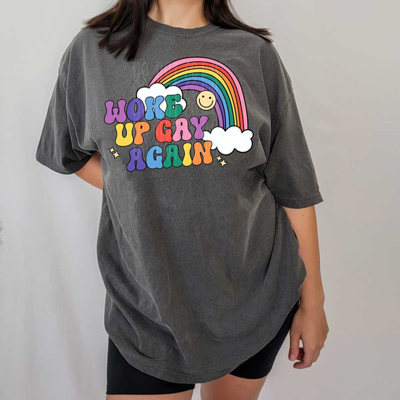 Woke Up Gay Again DTF Heat Transfer, colorful graphic T-shirt with rainbow, clouds, and happy face design.