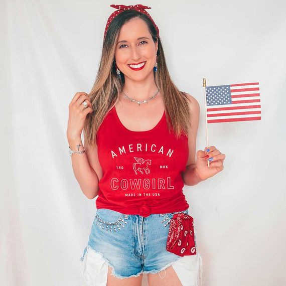 American Cowgirl DTF Heat Transfer, woman wearing red tank top with American Cowgirl design, holding small American flag, patriotic style.