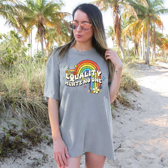 Equality Hurts No One DTF Heat Transfer, woman wearing a gray t-shirt with rainbow and colorful text design outdoors.