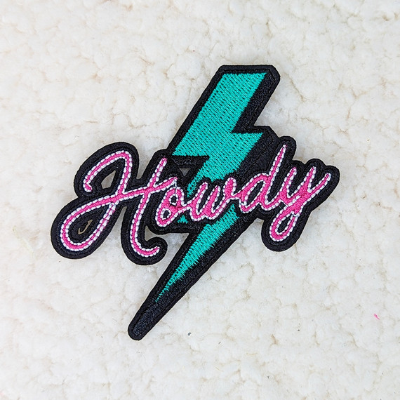 Howdy Lightning Bolt Embroidered HAT/POCKET Patch, a colorful embroidered patch featuring a turquoise lightning bolt and the word 'Howdy' in pink script outlined in black.