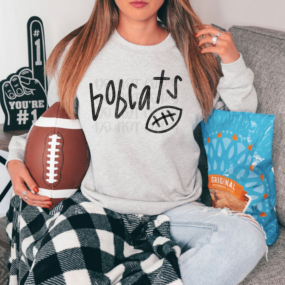 Bobcats Football DTF Heat Transfer, a woman wearing a gray sweatshirt with 'Bobcats' and a football graphic, holding a football, illustrating the product for sports team apparel customization.