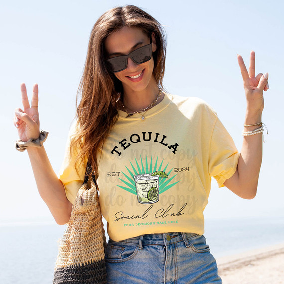 Tequila Social Club DTF Heat Transfer, graphic design of a cocktail with lime slices and sunburst background printed on a yellow t-shirt worn by smiling woman at the beach.