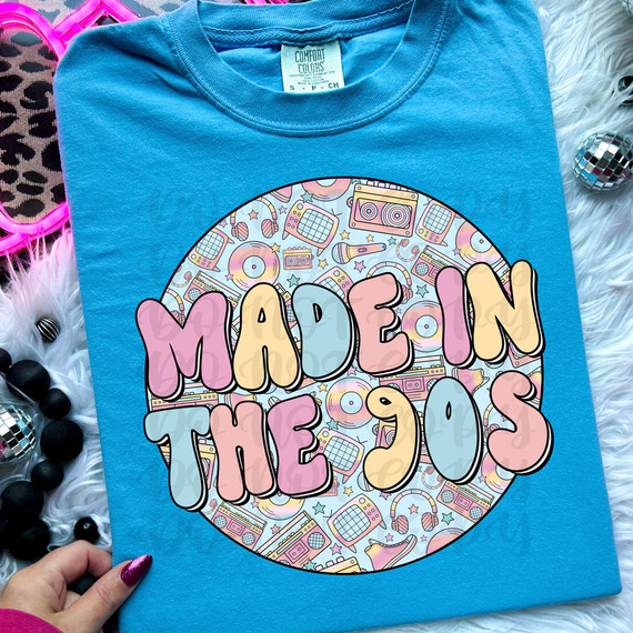 Made In The 90s DTF Heat Transfer, colorful graphic t-shirt design with 90s-inspired icons and the phrase 'Made In The 90s' on blue fabric.