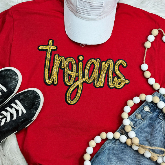Trojans Gold Sequin Patch, a decorative gold sequin patch with the word 'Trojan' embroidered on a red t-shirt.