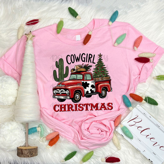 Cowgirl Christmas DTF Heat Transfer, pink T-shirt with a festive Christmas design featuring a red vintage pickup truck, a Christmas tree, cactus, and holiday decorations.
