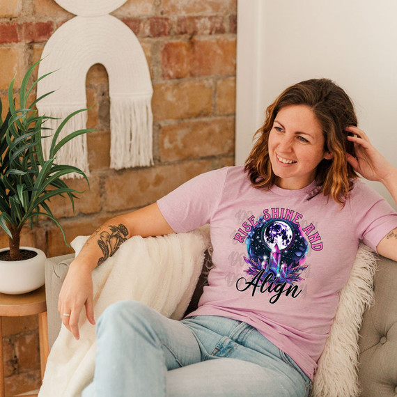 Rise, Shine And Align DTF Heat Transfer, colorful graphic T-shirt design with a moon, stars, and crystals on a woman sitting on a sofa.