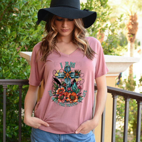 I Am The Way. The Truth. The Life DTF Heat Transfer, a colorful design with flowers, cacti, and a cross, printed on a pink T-shirt worn by a woman outdoors.