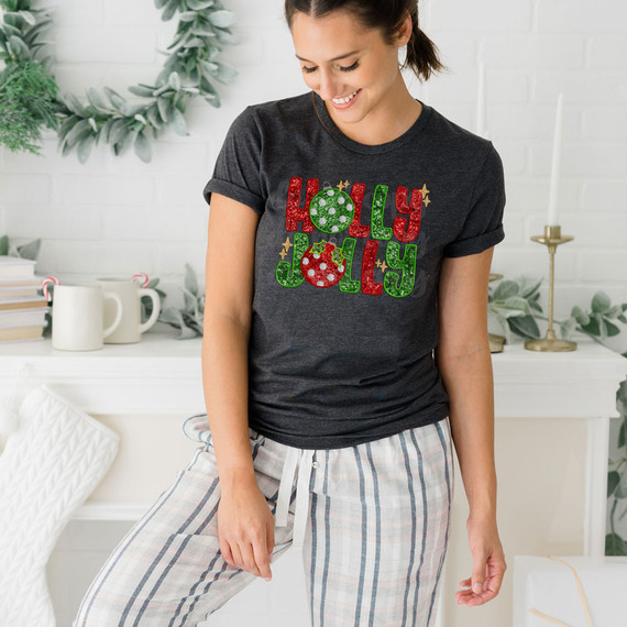 Holly Jolly Faux Embroidered Sequins DTF Heat Transfer, woman wearing holiday-themed T-shirt with festive 'Holly Jolly' design in red, green, and white sequins, in a cozy home setting.