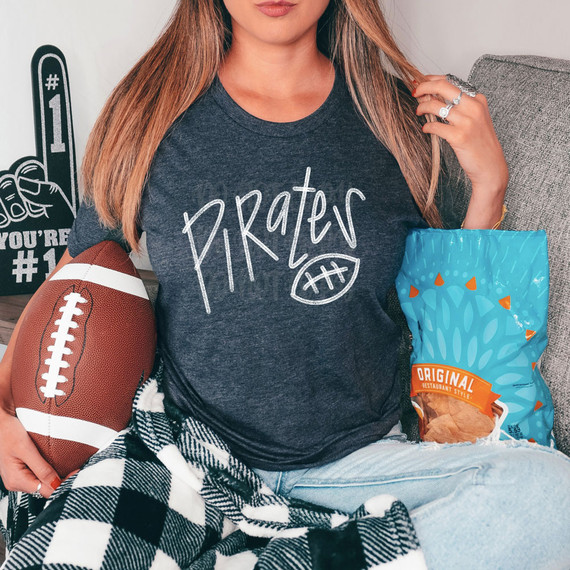 Pirates Football WHITE DTF Heat Transfer, image of a woman wearing a grey t-shirt with the word 'Pirates' and a football graphic, holding a football, sitting next to a bag of chips.