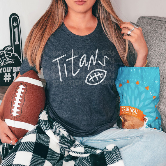 Titans Football WHITE DTF Heat Transfer, woman wearing a T-shirt with 'Titans' print and football illustration, holding football and sitting next to snack bag, showcasing sports-themed apparel.