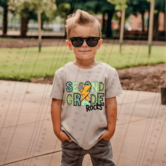 Second Grade Rocks Blue/Green DTF Heat Transfer, colorful graphic tee shirt with rocks and lightning bolt design worn by a young boy at the park.