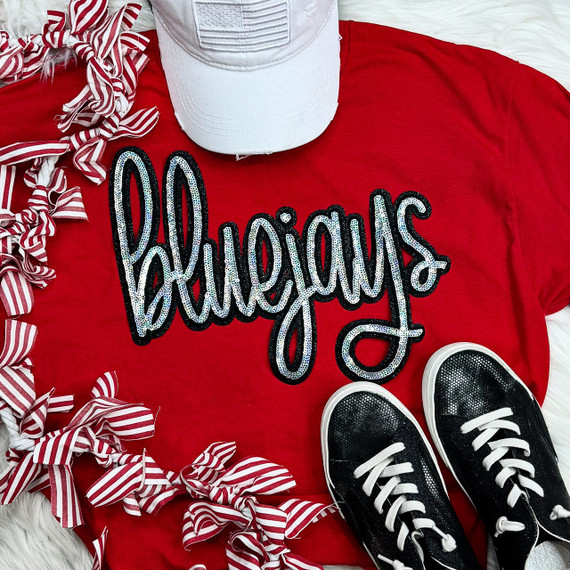 Bluejays Sequin Patch, a blue and white glittery sequin patch spelling 'Bluejays' on a red t-shirt surrounded by striped ribbon bows, white cap, and black sneakers.