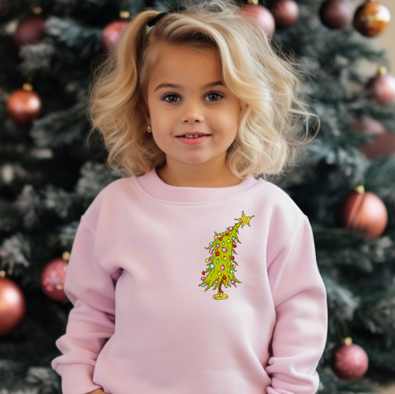 Little Tree Hat/Pocket Screen Print Heat Transfer, Christmas tree design on a pink sweatshirt worn by a young girl in front of a decorated Christmas tree.